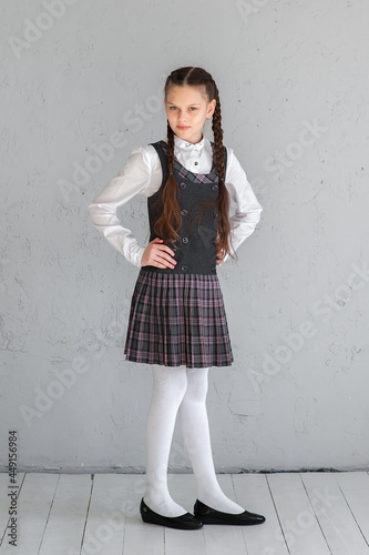 Cute smiling schoolgirl in uniform standing on grey background