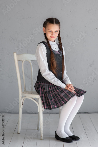 Portrait of a cute girl in a school uniform sitting on a chair.