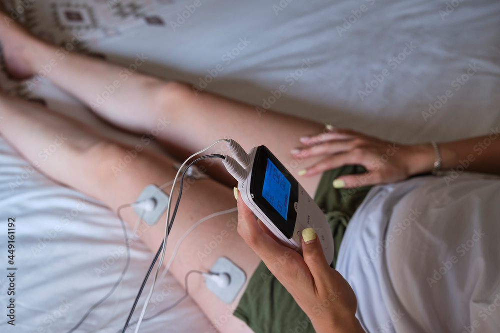 electrostimulation treatment at home, electrodes on the leg of an unrecognizable woman, getting a treatment of tens, ems or massages to improve muscle health and improve blood circulation. 