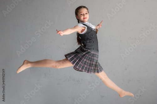Fotografia Cute smiling schoolgirl in uniform jumping on gray background