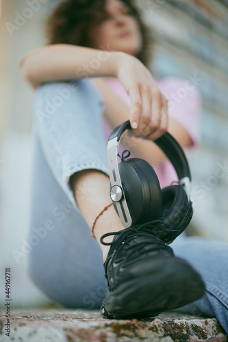 Close up of young woman sitting on the bench and holding headphones. Selective focus on the headphones.