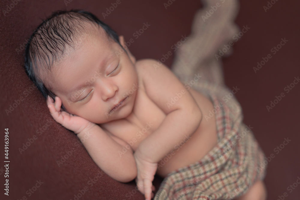 newborn baby boy sleeping peacefully on brown blanket with checkered cloth on brown background.new born portrait. black hair baby newborn baby boy sleeping peacefully on brown blanket with checkered cloth on brown background.new born portrait. black hair baby