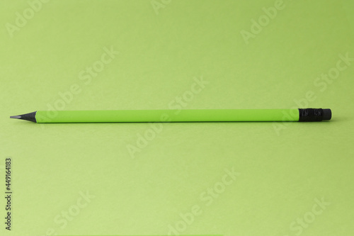 Sharp simple pencil lying on green background closeup