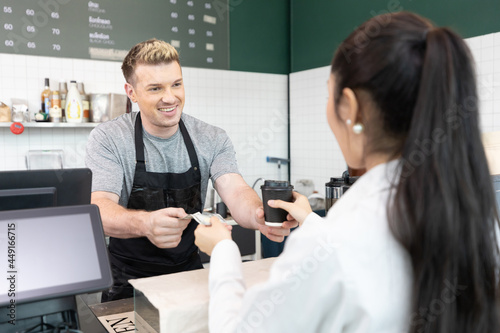 male barista giving a cup of coffee and getting cash from customer in cafe or coffee shop