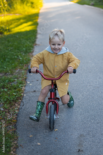 Fototapeta Naklejka Na Ścianę i Meble -  Cheerful boy in a yellow jacket rides a bicycle at the street