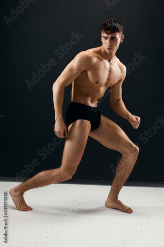 sporty man with a pumped up muscular body in black panties posing against a dark background
