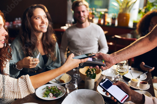 Friends paying contactlessly in restaurant photo