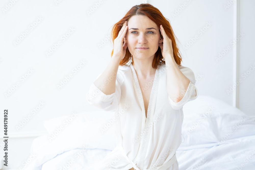 Beauty portrait smiling ginger woman middle age in silk robe doing a facial massage in light room Beauty portrait smiling ginger woman middle age in silk robe doing a facial massage in light room