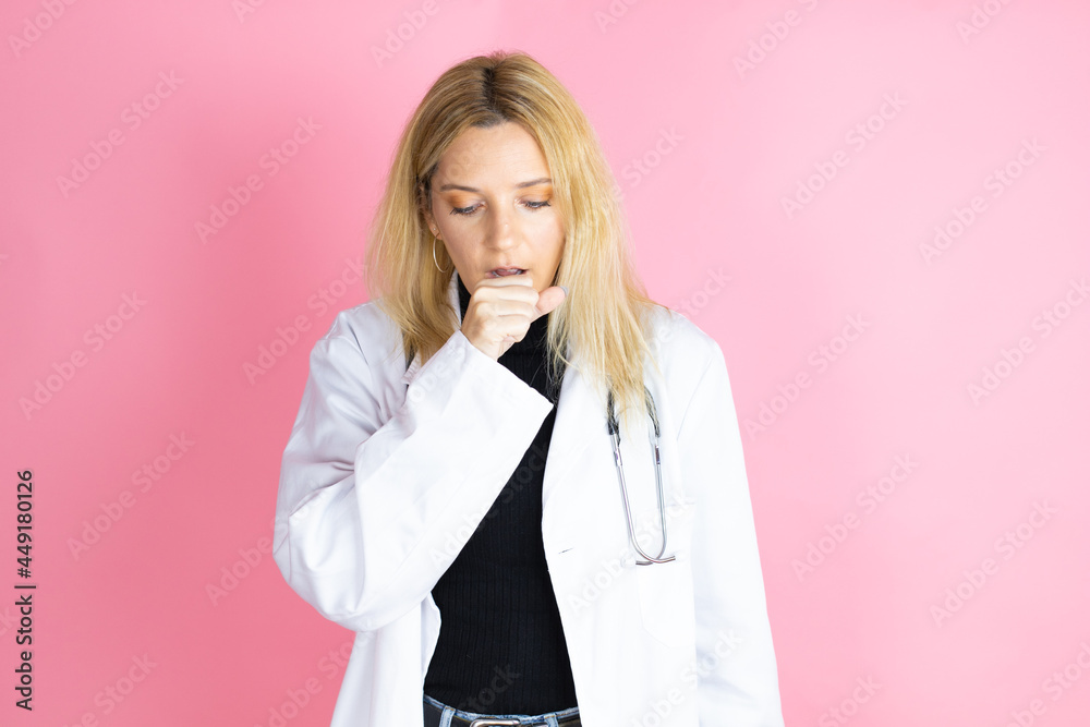 Young blonde doctor woman wearing stethoscope standing over isolated pink background with her hand to her mouth because she's coughing Young blonde doctor woman wearing stethoscope standing over isolated pink background with her hand to her mouth because she's coughing
