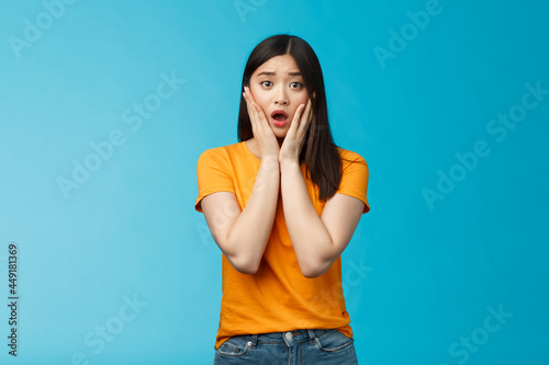 Shocked concerned young asian girl look empathy camera, gasping open mouth worried, frowning upset hear frustrating news, pitty feel sorry for friend, touch cheeks speechless, stand blue background photo