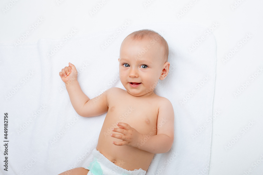 A baby boy in a diaper is lying on his back on a white background, looking at the camera and smiling. view from above. Changing baby diapers and skin care. A baby boy in a diaper is lying on his back on a white background, looking at the camera and smiling. view from above. Changing baby diapers and skin care.