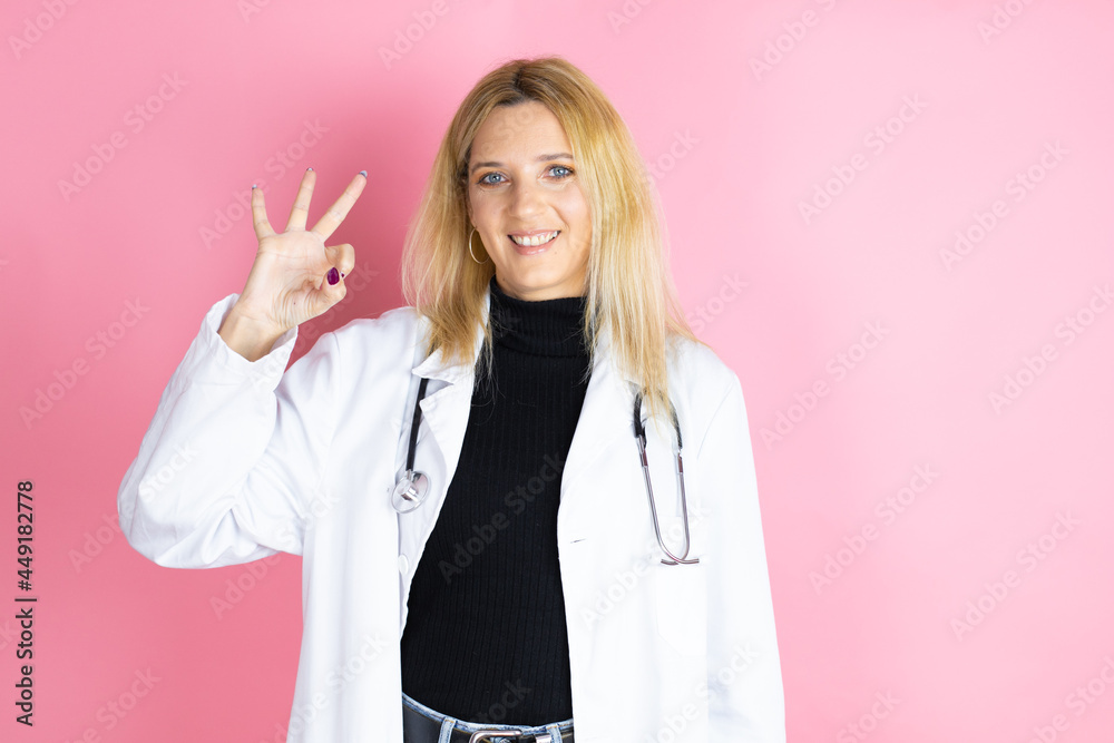 Young blonde doctor woman wearing stethoscope standing over isolated pink background doing ok sign with fingers and smiling, excellent symbol Young blonde doctor woman wearing stethoscope standing over isolated pink background doing ok sign with fingers and smiling, excellent symbol
