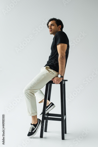 full length of young man in black t-shirt sitting on chair on grey
