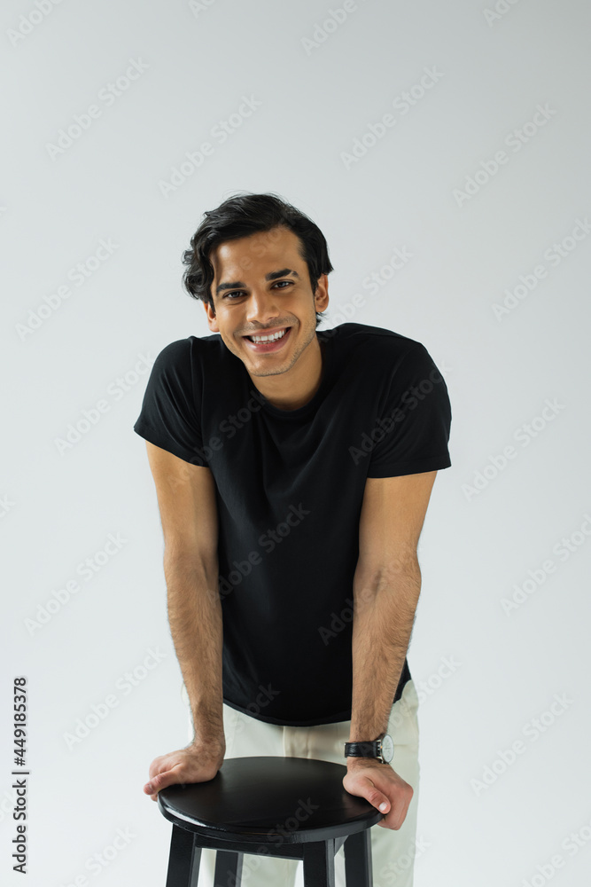portrait of cheerful young man looking at camera and leaning on chair isolated on grey portrait of cheerful young man looking at camera and leaning on chair isolated on grey