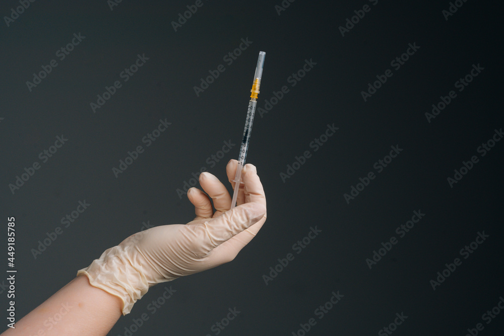 Close-up hands of unrecognizable nurse wearing white latex gloves holding syringe on isolated black background. Studio shot of healthcare worker with protective gloves is holding syringe, closeup. Close-up hands of unrecognizable nurse wearing white latex gloves holding syringe on isolated black background. Studio shot of healthcare worker with protective gloves is holding syringe, closeup.