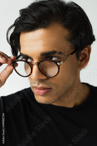 stylish man adjusting eyeglasses isolated on grey