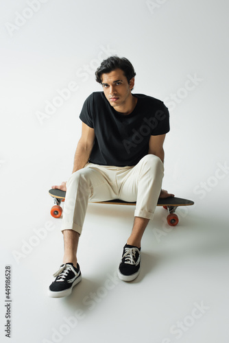 serious young man in black t-shirt sitting on longboard on grey