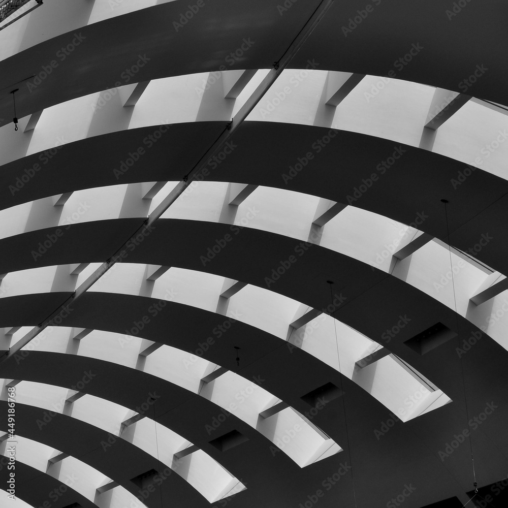 A curved ceiling of a huge building. An abstract black and white photo of an interior building. A curved ceiling of a huge building. An abstract black and white photo of an interior building.