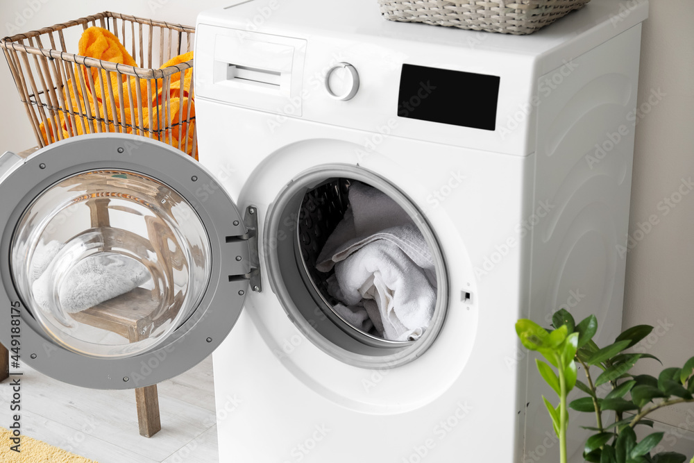 Modern washing machine with laundry in bathroom