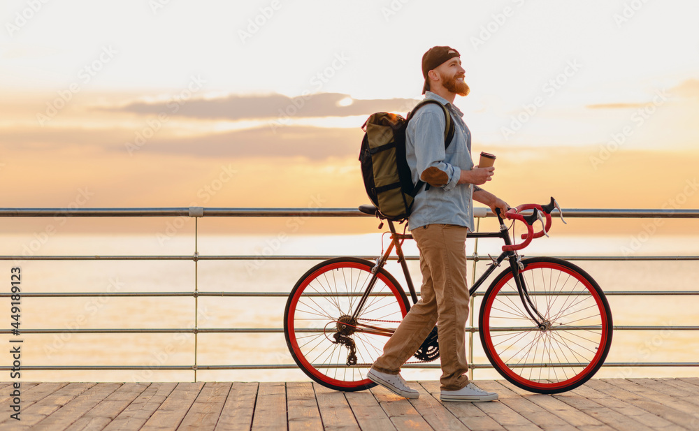 Fototapeta premium handsome bearded man traveling with bicycle in morning sunrise by the sea