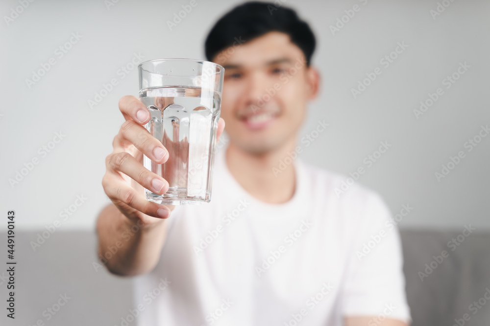 handsome asian man drinking a glass of water on the sofa at living room . handsome asian man drinking a glass of water on the sofa at living room .