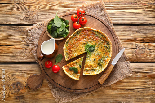 Board with tasty spinach tart and ingredients on wooden background