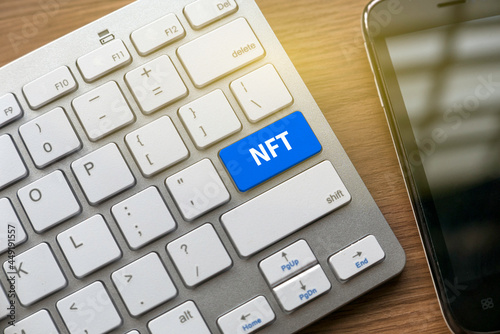 NFT or non fungible token concept with keyboard and blue button and a mobile phone on a desk. photo