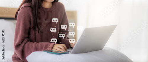 Woman using laptop in bed in bedroom for social network chat with chat box icons. concept of using the Internet in social networks and work from home. photo