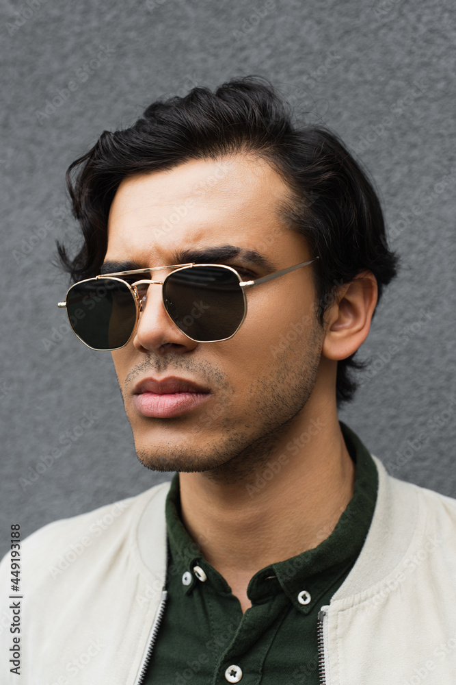 Obraz premium portrait of young man in stylish sunglasses posing near grey wall