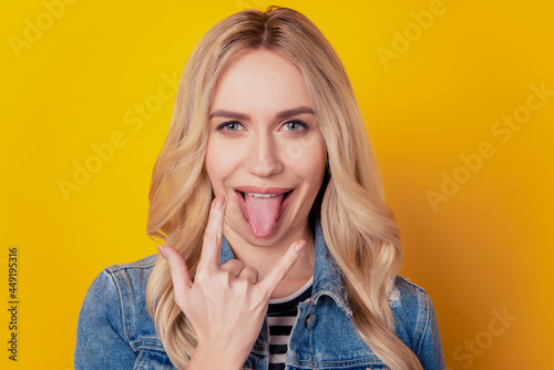 Portrait of funky positive rock fan girl showing horns sign protrude tongue on yellow background