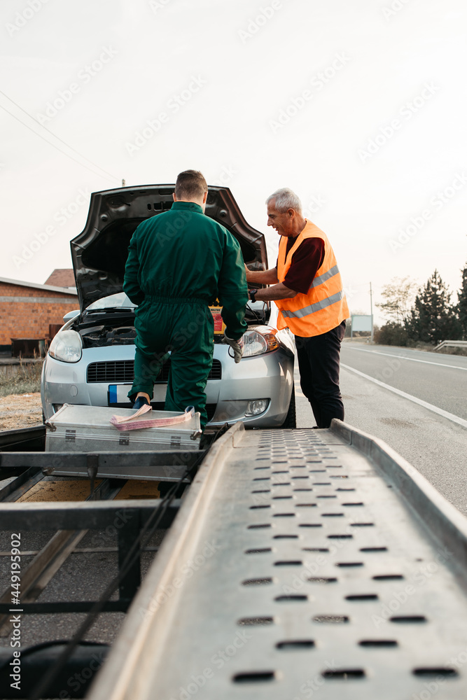 Two road assistant workers in towing service trying to start car engine with jump starter and energy station with air compressor. Roadside assistance concept. Two road assistant workers in towing service trying to start car engine with jump starter and energy station with air compressor. Roadside assistance concept.