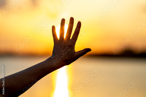A woman reaches out to the sky with her hand and covers the sun, the sun's rays pass through her hand. The concept of receiving light, energy and joy from nature. An image of an evening sunset. .