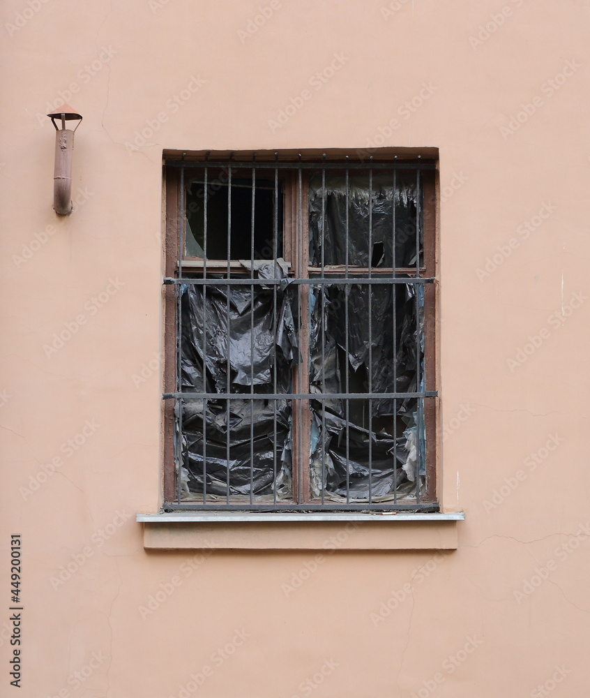 A barred window with torn black plastic