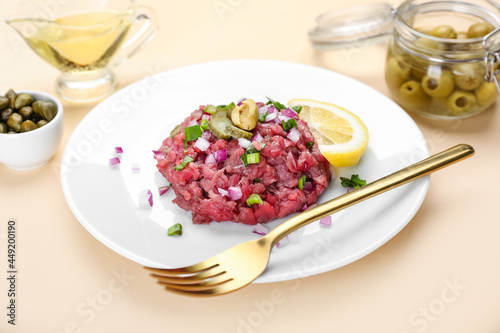 Plate with tasty beef tartare and olives on color background, closeup