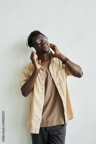 African young man in wireless headphones leaning on the wall enjoying the music with eyes closed