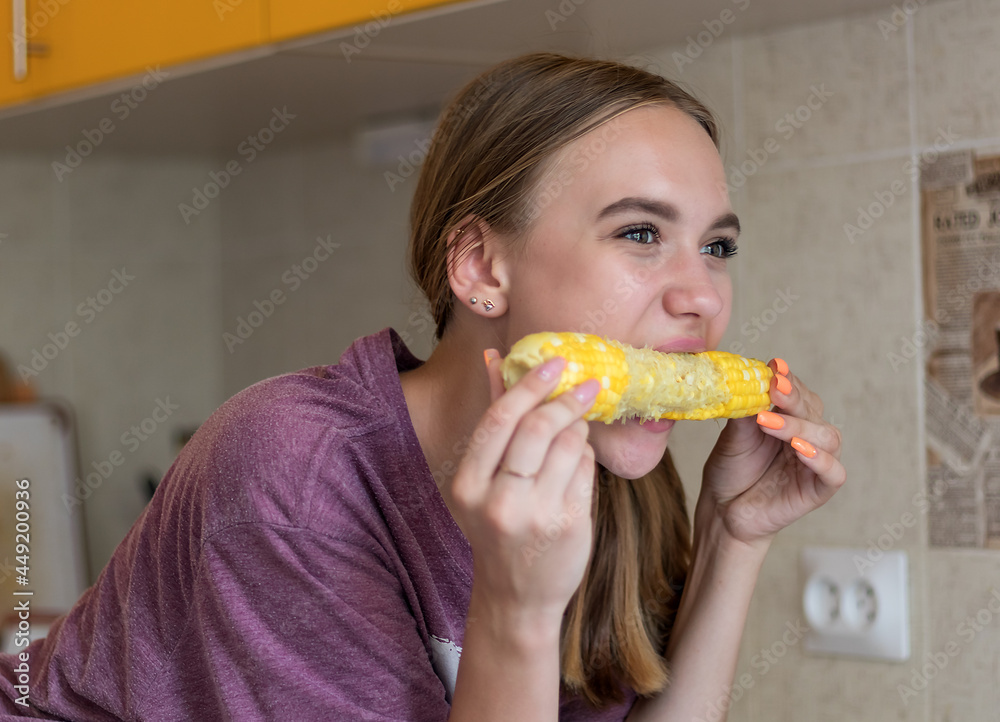 young girl with appetite eats an ear of boiled corn in the kitchen, woman close-up portrait young girl with appetite eats an ear of boiled corn in the kitchen, woman close-up portrait