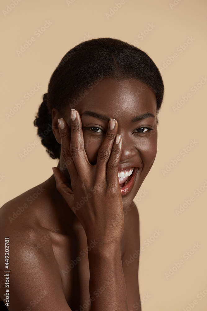Portrait close up of beautiful african girl. Smiling young woman touch her clean face and looking at camera. Concept of face skin care. Isolated on beige background. Studio shoot Portrait close up of beautiful african girl. Smiling young woman touch her clean face and looking at camera. Concept of face skin care. Isolated on beige background. Studio shoot