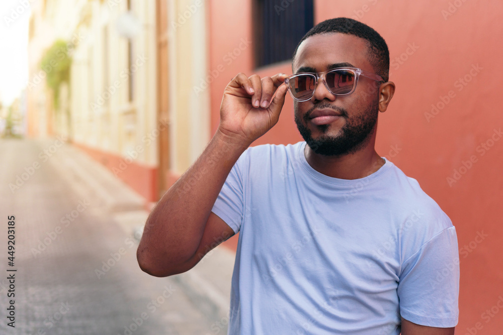 African man with sunglasses walking in the city street looking at the camera.