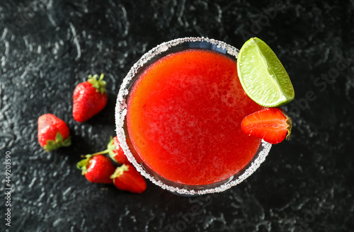 Glass of strawberry daiquiri cocktail and berries on dark background photo