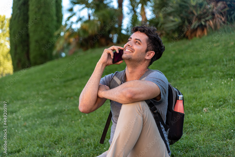 Young latin man sitting in the grass talking by mobile phone.