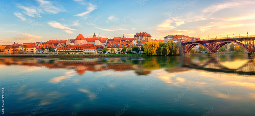 Amazing view of Maribor Old city, Main bridge (Stari most) on the Drava river at sunrise, Slovenia. Scenic cityscape with blue sky and reflection, travel background for wallpaper or guide book