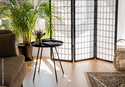 Home living room with wood and paper divider screen blocking sun from window, black metal accent table and sofa, natural colors. photo