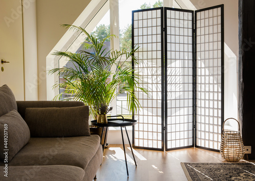 Home living room with wood and paper divider screen blocking sun from window, black metal accent table and sofa, natural colors. photo