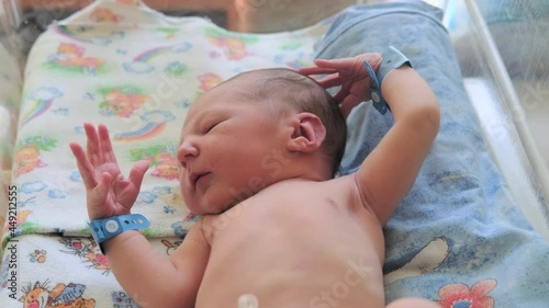 A newborn baby raises his hands up in the crib of the maternity hospital, Moro reflex
