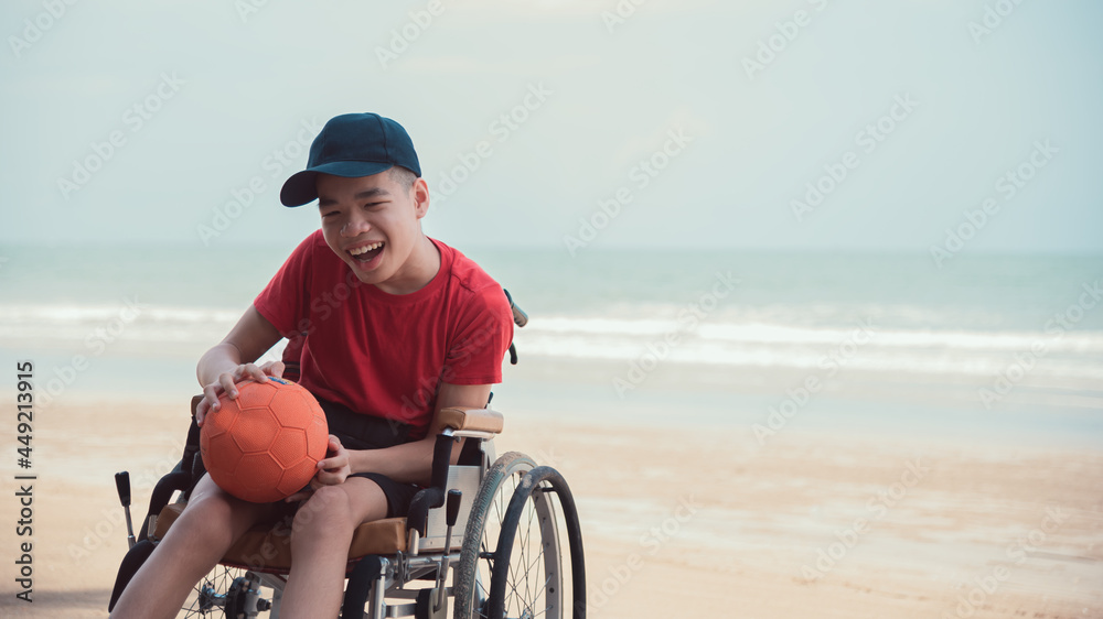 Happy disabled teenage boy on wheelchair playing a ball, Activity outdoors with father on the beach background, People having fun and diverse people concept. Happy disabled teenage boy on wheelchair playing a ball, Activity outdoors with father on the beach background, People having fun and diverse people concept.