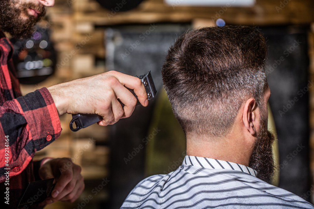 Hands of barber with hair clipper, close up. Haircut concept. Hipster client getting haircut. Man visiting hairstylist in barbershop. Barber works with hair clipper. Hipster client getting haircut