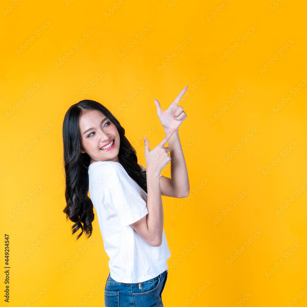 beautiful cute Asian woman smiling and pointing finger to empty copy space , blank space for advertising isolated on yellow background