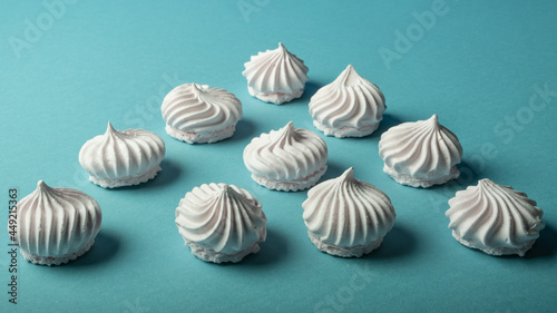 Beautifully laid out snow-white meringue cookies on a light turquoise background. Light dessert.