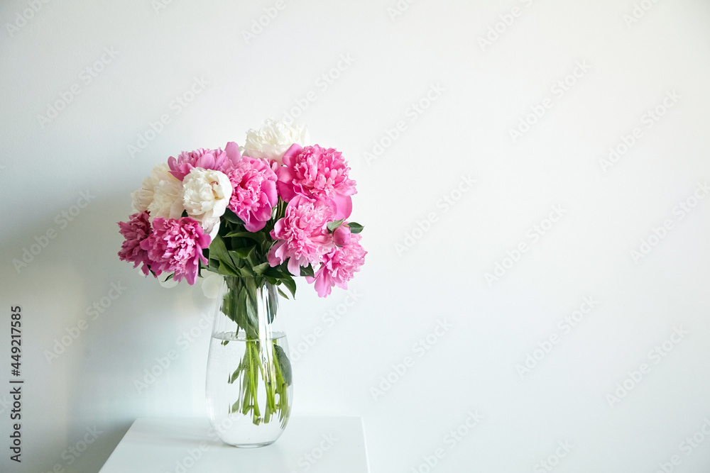 Empty white wall with pink flowers. Peonies in a glass vase in a bright interior