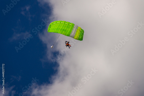 Skydiver under the canopy green of the parachute against a blue sky and white clouds photo